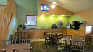 A dining area with wooden tables and chairs, a kitchen counter with appliances, and a television mounted on the wall. - Super Davneport Inn & Suite (Davenport)