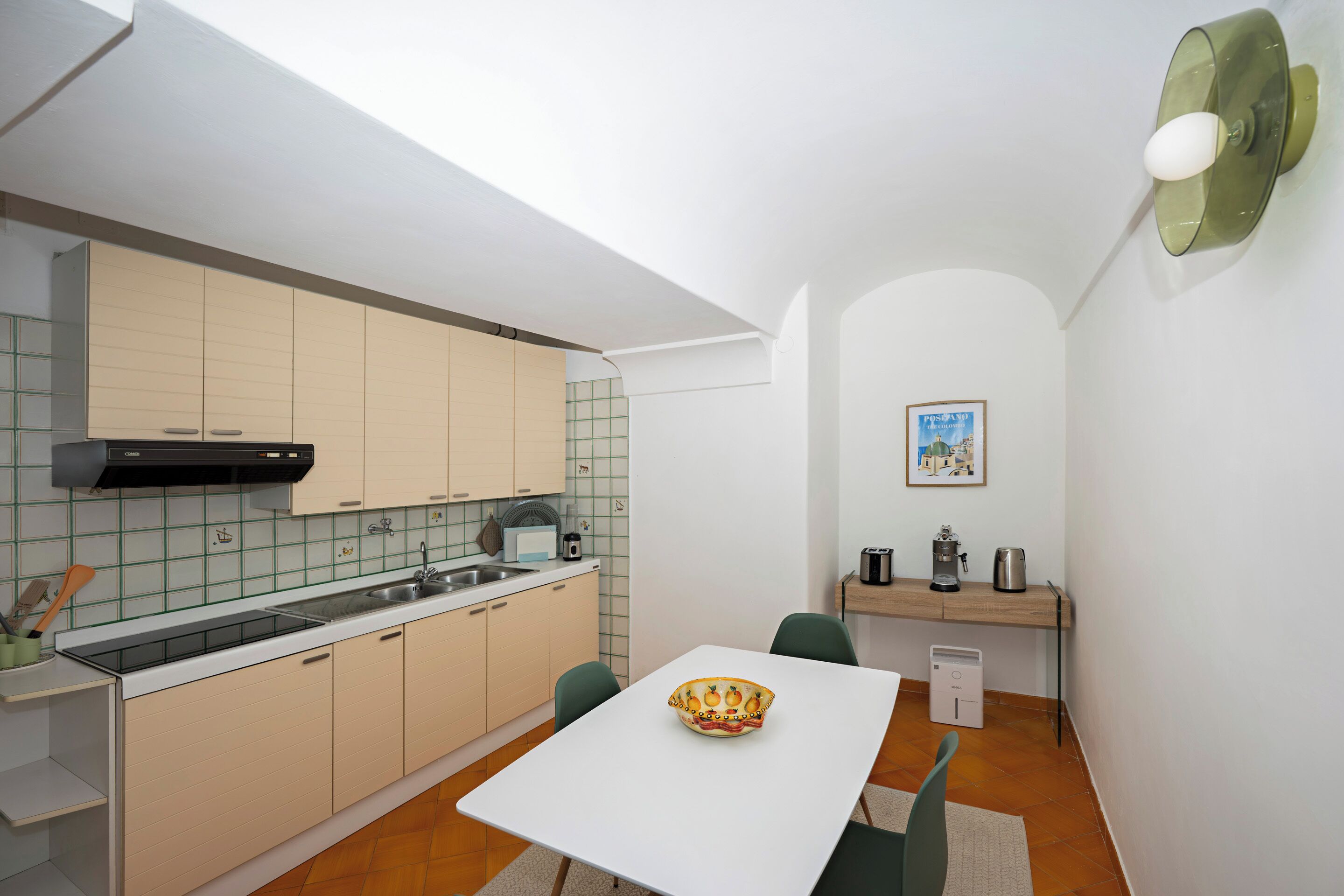 Una cocina compacta con encimera blanca, armarios color beige y un pequeño comedor con mesa y sillas blancas.
