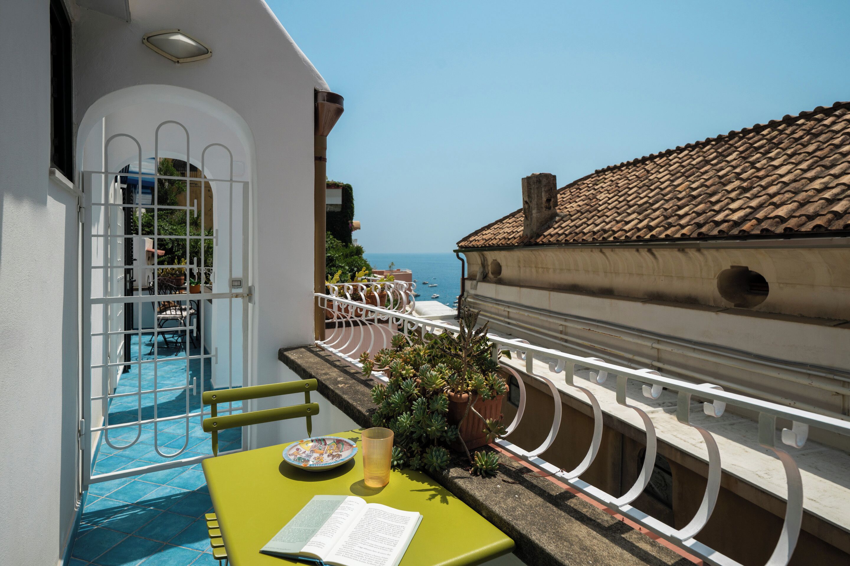 Un balcón con vista al mar, una piscina y una mesa con un libro y un plato.