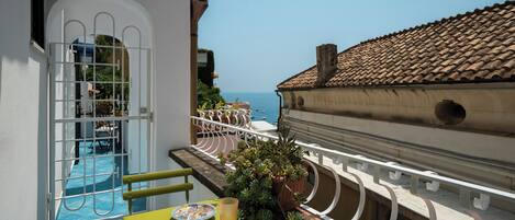 Un balcón con vista al mar, una piscina y una mesa con un libro y un plato.