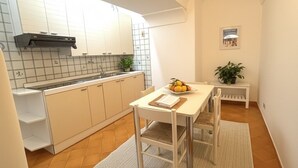 A compact kitchen with white cabinets, a dining table with chairs, a small bench, and a potted plant. - De Vivo Realty - The Colombo Positano (Positano)