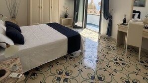 A hotel room with a bed, a desk, a chair, a wardrobe, a TV, and a balcony with a view. - De Vivo Realty - The Colombo Positano (Positano)