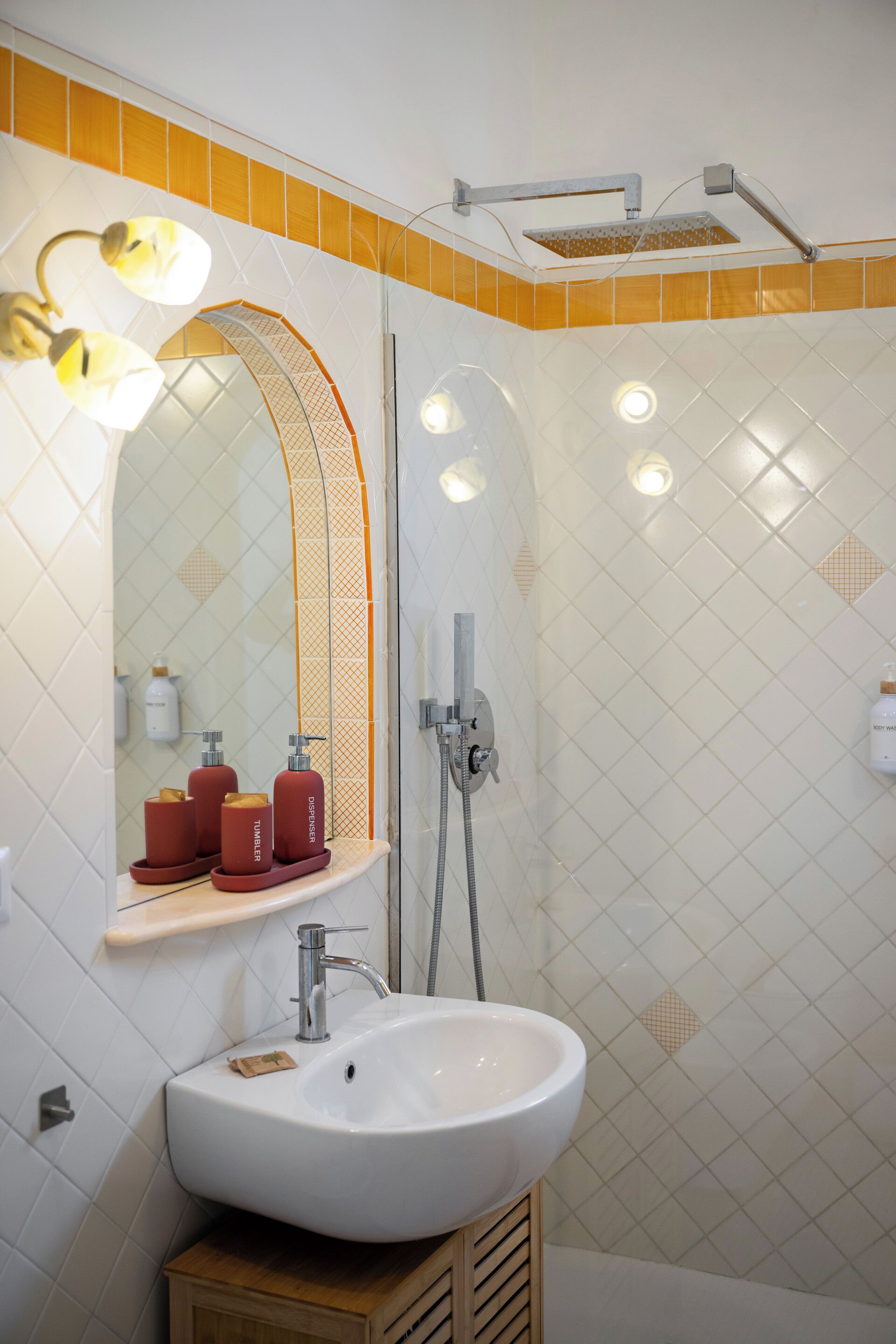 A bathroom with a white sink, a mirror with lights, a shower, and a towel rack.