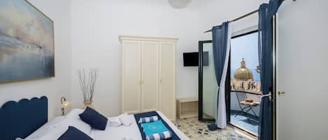 Habitación de hotel con cama, armario, televisor y balcón con vistas.