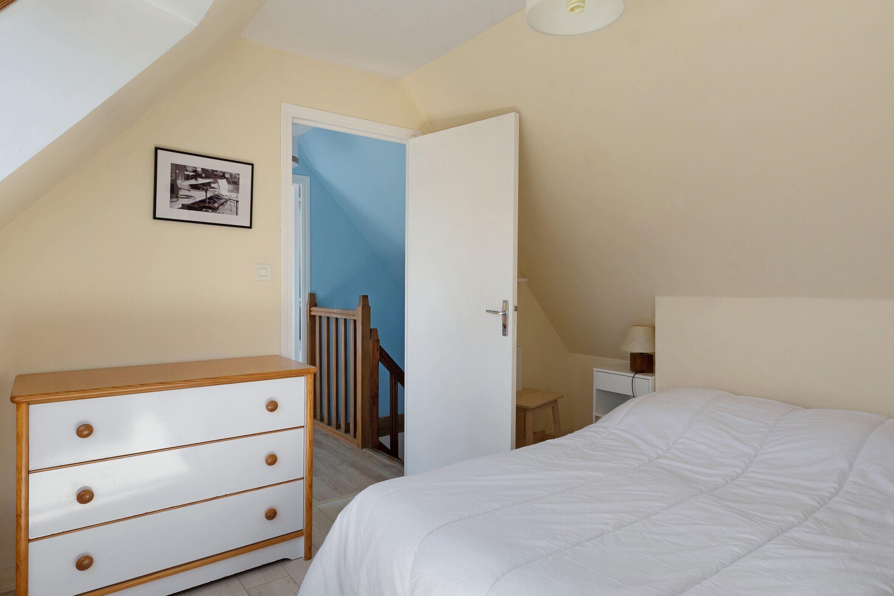 Une chambre à coucher comprenant un lit, une commode, un bureau et un escalier menant à une autre pièce.