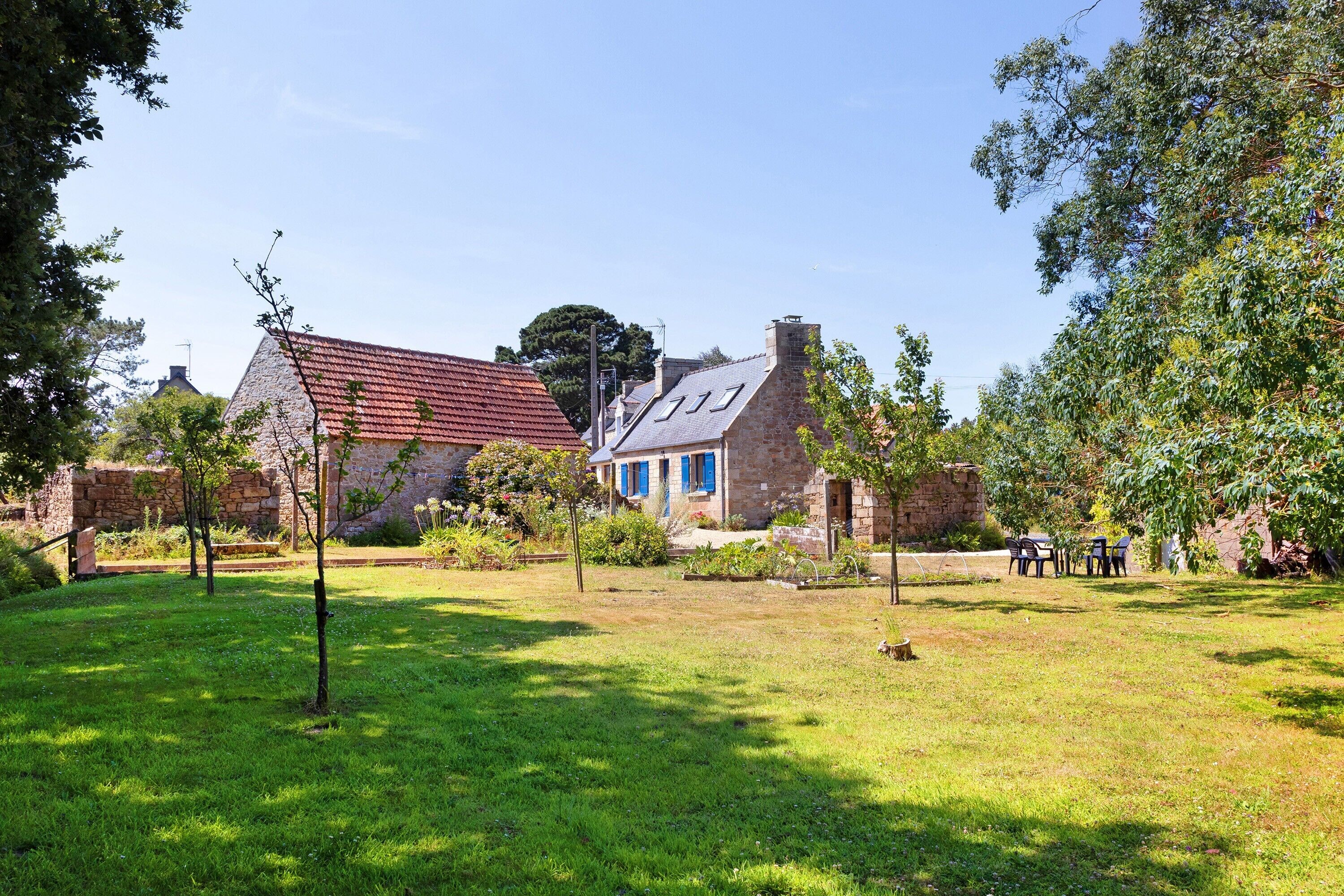 A stone building with a red-tiled roof, surrounded by a well-maintained lawn and trees.