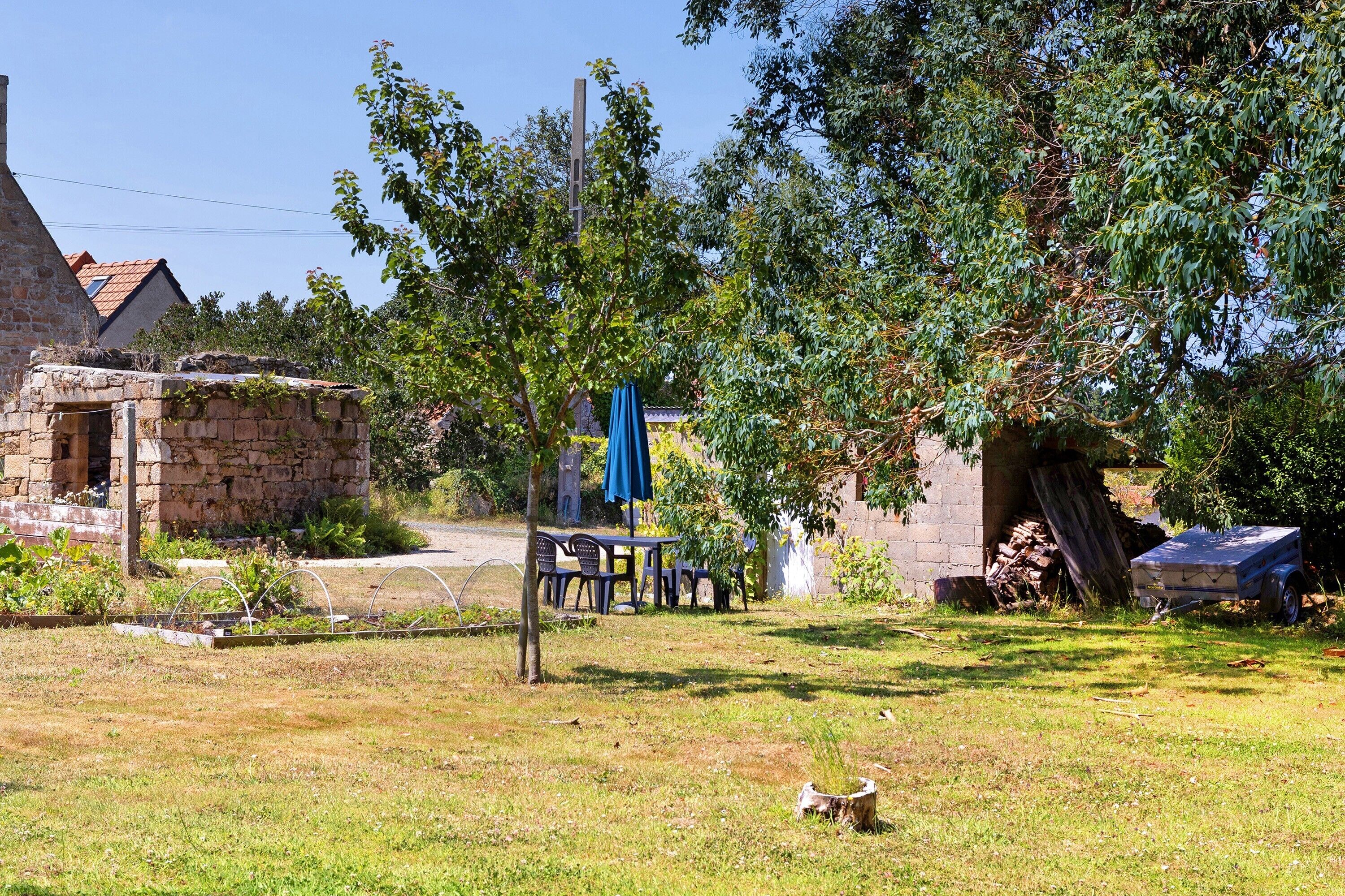 Un entorno rústico al aire libre con un edificio de piedra, una mesa con sillas y un árbol grande.