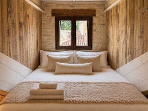 A bedroom with a wooden sloped ceiling, a window with a view of a tiled roof, a bed with pillows, and a folded towel on the bed. - Cà Livia by Venicescape (Venice)