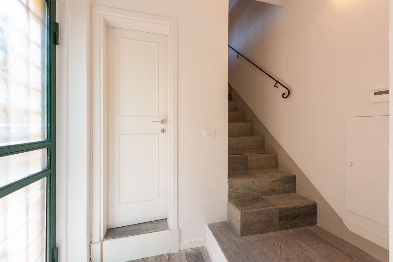 Eine Treppe mit Handlauf, eine weiße Tür und ein Fenster mit Jalousien.