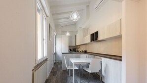 A modern kitchen with white cabinetry, a dining table with chairs, pendant lighting, and a view to the dining area. - Vettori Hideaway by MMega Homes and Villas (Florence)