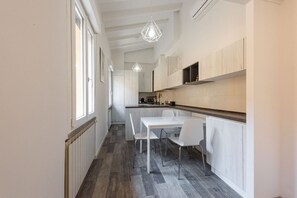 A modern kitchen with white cabinetry, a dining table with chairs, pendant lighting, and a view to the dining area. - Vettori Hideaway by MMega Homes and Villas (Florence)