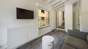 A modern interior with a flat-screen TV mounted on the wall, a radiator, a window with a metal railing, and a sofa. - Vettori Hideaway by MMega Homes and Villas (Florence)