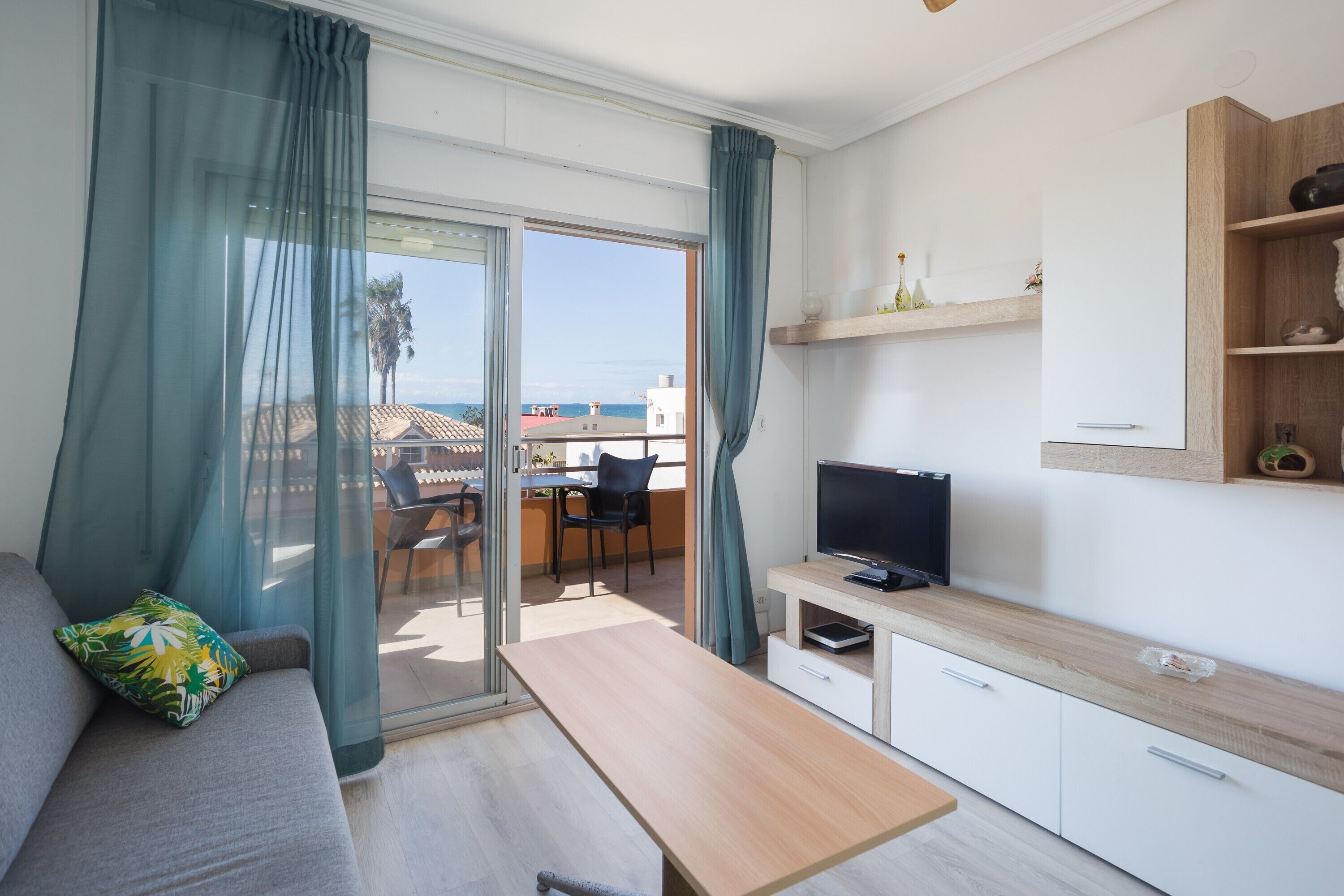 Una sala de estar moderna con un sofá, un televisor, una mesa de madera y un ventanal corredizo que da a un espacio exterior.