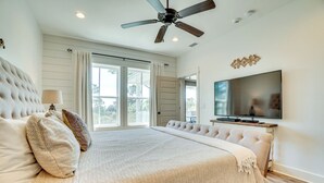 Een slaapkamer met een groot bed, een plafondventilator, een televisie en uitzicht door het raam.