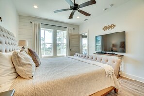 Ein Schlafzimmer mit einem großen Bett, einem Deckenventilator, einem Fernseher und Blick durch das Fenster.