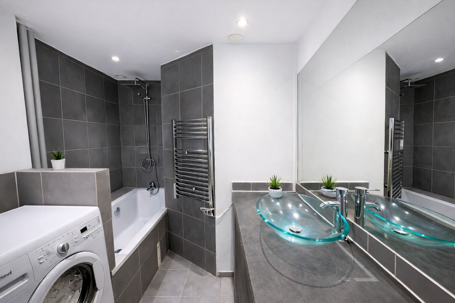 Un baño moderno con lavadora blanca, bañera con mampara de vidrio y un espejo grande.