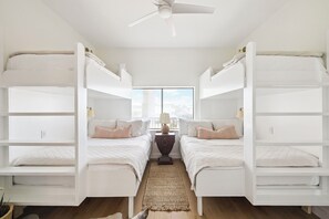 A room with two bunk beds, a central nightstand with a lamp, and a view of the sky through a window. - Beachfront Condo w/ Community Pool and Elevator (Santa Rosa Beach)