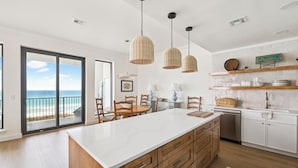 Una cocina moderna con una isla grande, luces colgantes y vista a la playa.