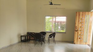 A room with a ceiling fan, a window with a view of greenery, a door with decorative panels, and a tiled floor.