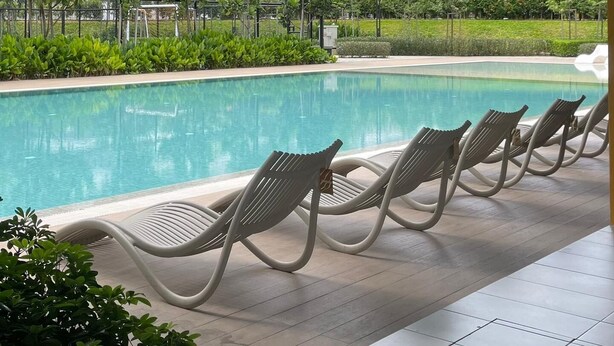 Un área de piscina moderna con sillas de descanso, una piscina cristalina y vistas a edificios altos.