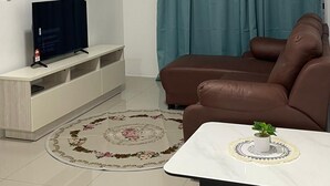 Una sala de estar con sofá, mesa de centro, televisor sobre un mueble, aire acondicionado y ventilador de techo.