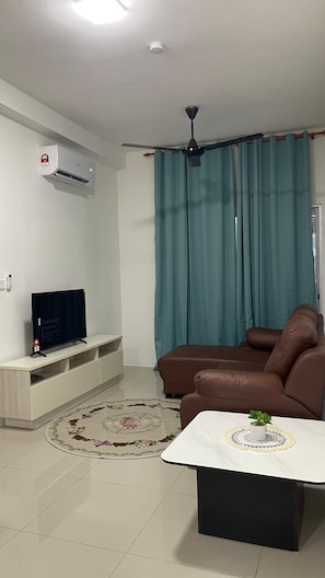 Uma sala de estar com sofá, mesa de centro, TV em um suporte, ar-condicionado e ventilador de teto.