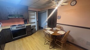 A compact kitchen with a stove, oven, and coffee maker. There is a dining table with chairs and a ceiling fan. - Inviting 1BR Near Boston -- Easy Transit -- Parking Included (Malden)