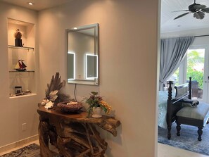 A wooden console table with a mirror, decorative items, and a view into a room with a chair and curtains.