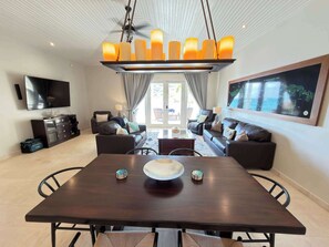 A modern living room with a dining area, a TV, and a large framed map on the wall. - Beachfront Villa | Ocean Views | Kayaks & SUPs (Cruz Bay)