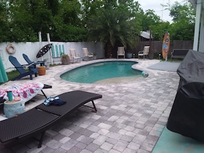 Ein Garten mit Swimmingpool, Liegestühlen und Grill.