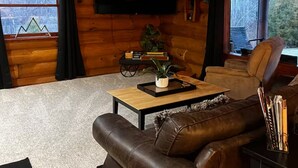Ein Holzblockhaus-Interieur mit einem Ledersofa, einem Couchtisch, einem Flachbildfernseher und einem Schild, das auf Wanderwege hinweist.