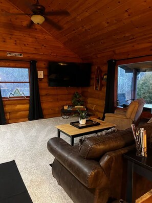 Ein Holzblockhaus-Interieur mit einem Ledersofa, einem Couchtisch, einem Flachbildfernseher und einem Schild, das auf Wanderwege hinweist.