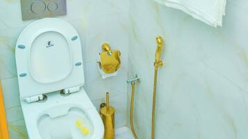 A bathroom with a toilet, a gold bidet, a towel rack, and a marble wall.
