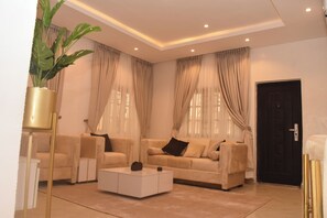 A living room with a beige sofa set, a white coffee table, and a potted plant.