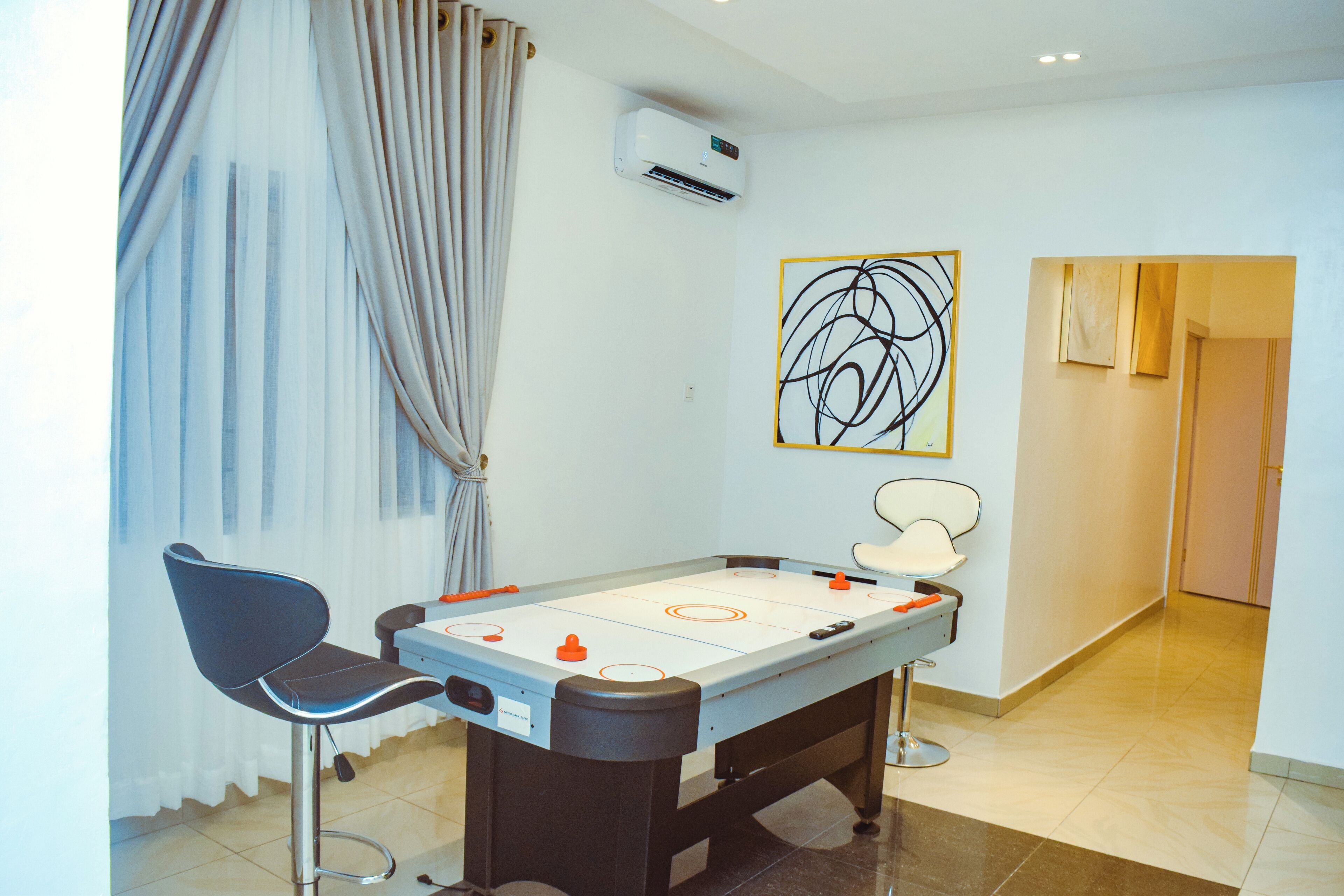 A room with a pool table, two chairs, a ceiling fan, an air conditioning unit, and a painting on the wall.