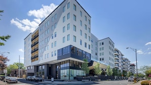 Ein modernes, mehrstöckiges Hotel mit einer markanten Glasfassade, einem gut sichtbaren Eingang mit Stufen und einem Parkplatz davor.