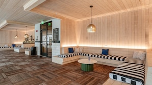 Eine moderne Lobby mit Holzwandverkleidung, einem Empfangstresen, Sitzbereichen und einem runden grünen Tisch.