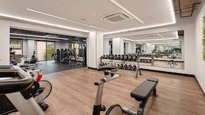 Ein Fitnessraum mit Trainingsgeräten, einer Bank und einem Spiegel, der die Geräte reflektiert.