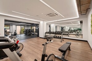 Ein Fitnessraum mit Trainingsgeräten, einer Bank und einem Spiegel, der die Geräte reflektiert.