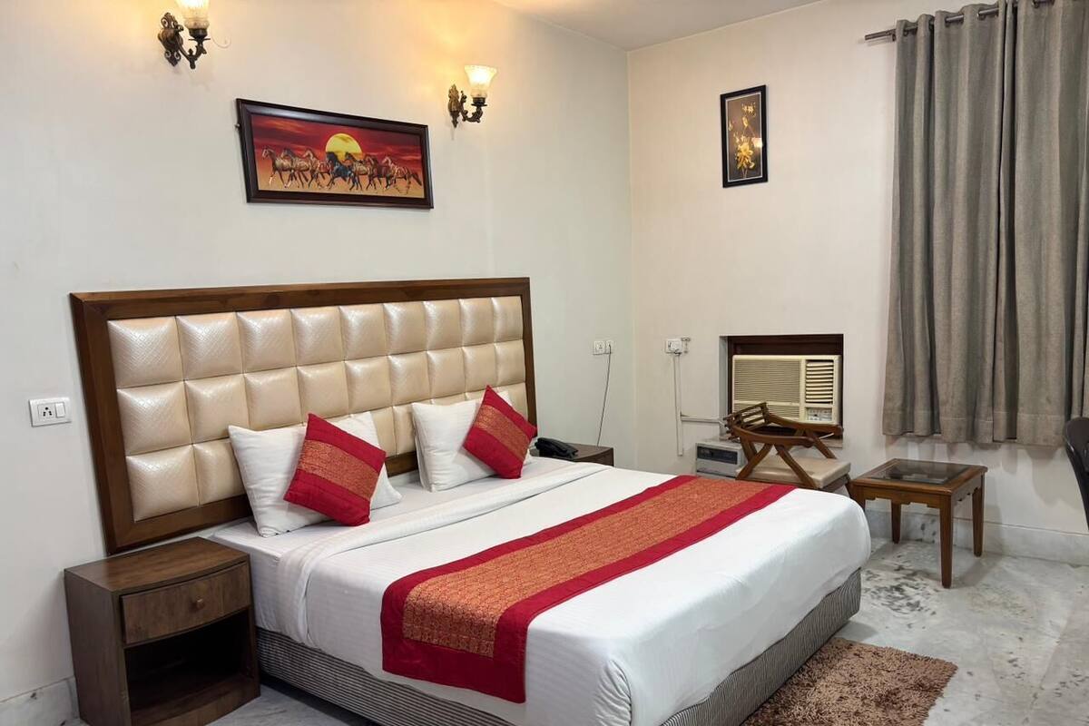 Una habitación de hotel con una cama grande, una mesita de noche, una silla, una pequeña mesa y una lámpara de pared.