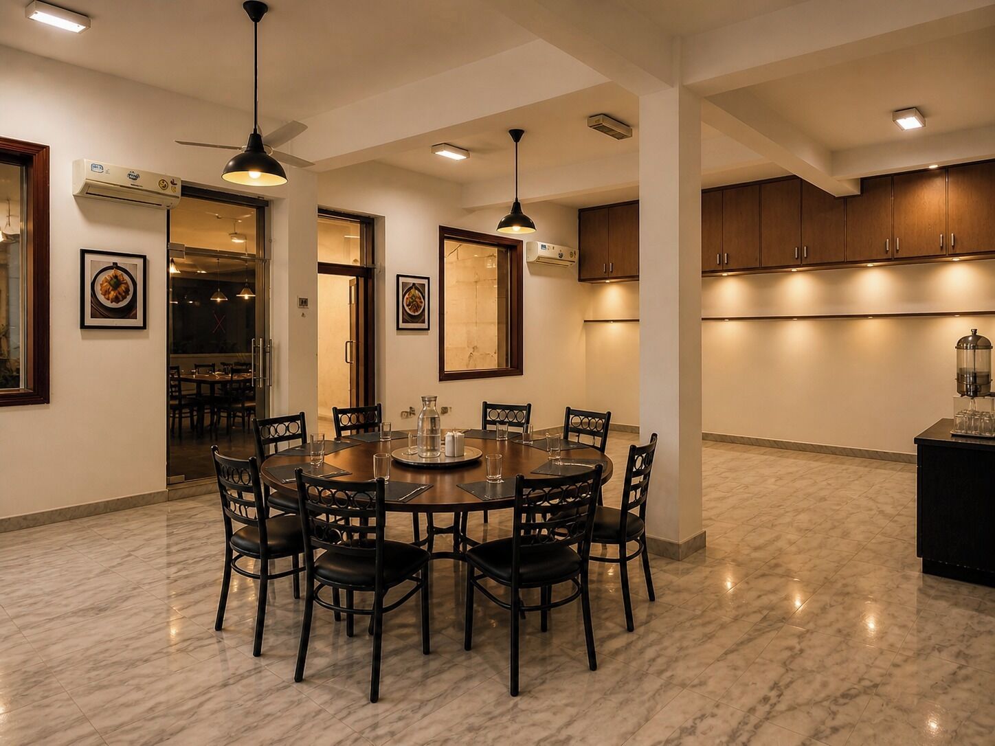 A dining area with a round table, chairs, pendant lights, and a kitchen area with cabinets.
