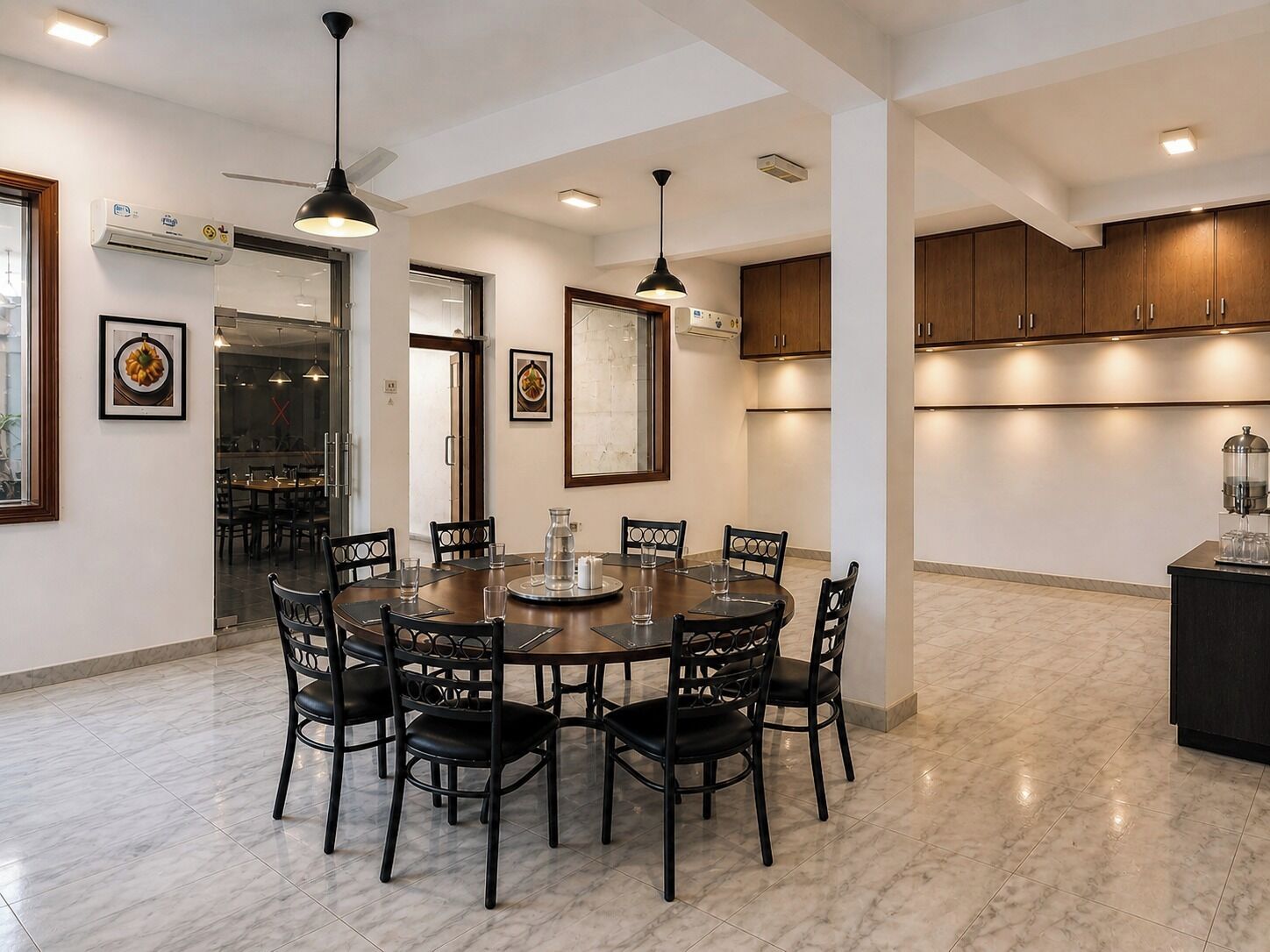 A modern dining area with a round table, black chairs, pendant lighting, and marble flooring.
