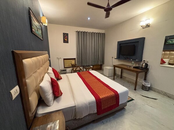 Habitación de hotel con cama, escritorio, televisor, ventilador de techo y ventana con cortinas.