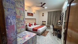 A hotel room with a bed, a desk, a chair, a ceiling fan, and a wall with a colorful abstract design. - The Lalit Vibes (Gurugram)