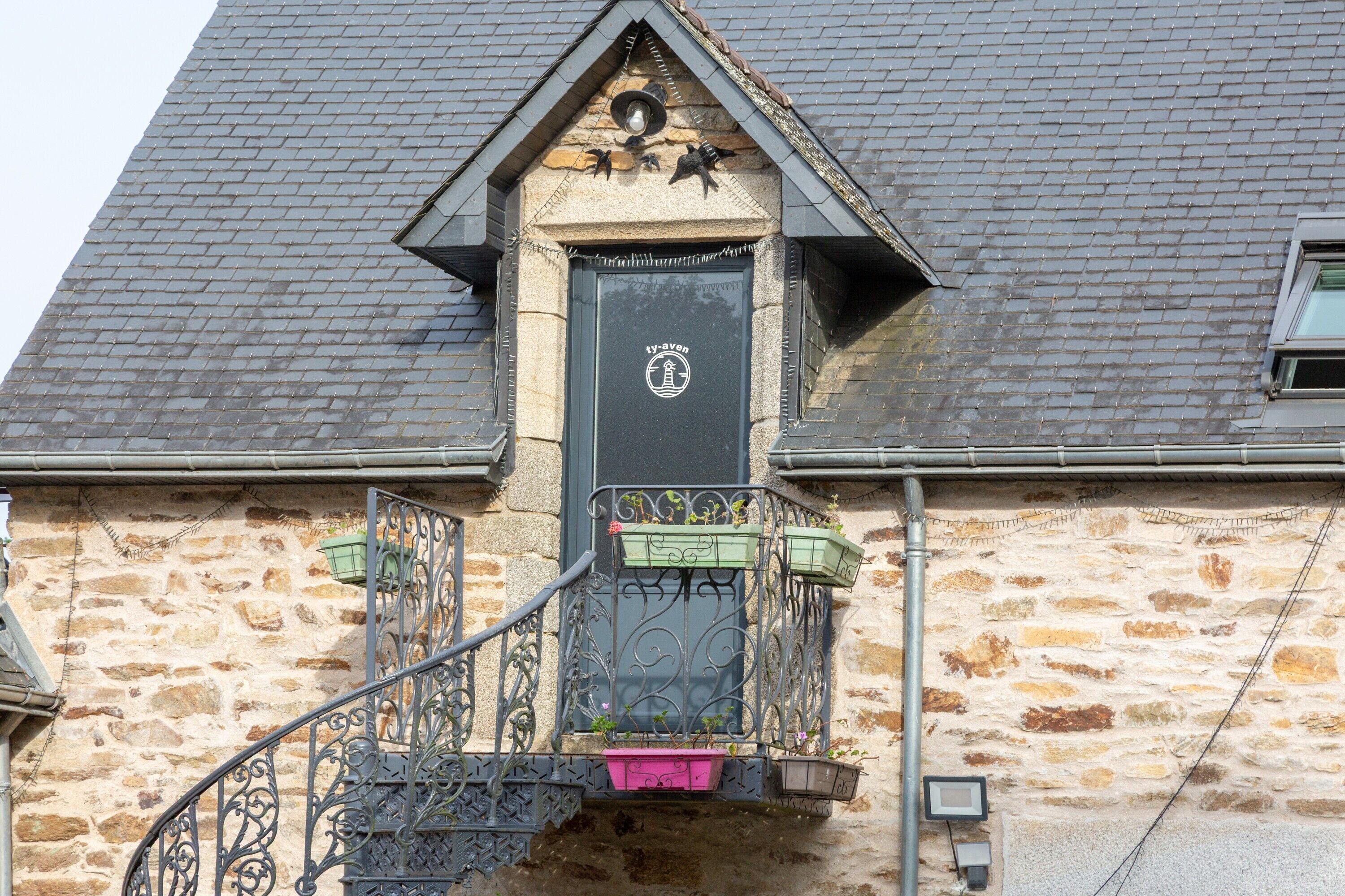 Een stenen gebouw met een zwarte deur, een klein balkon met metalen hekwerk en een trap die naar de ingang leidt.