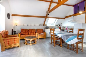 Un salón acogedor con muebles de madera, una mesa de comedor y una zona de cocina con ventanal.