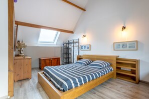 Un dormitorio con techo inclinado, una cama, muebles de madera, un mueble bajo y luces fijadas a la pared.