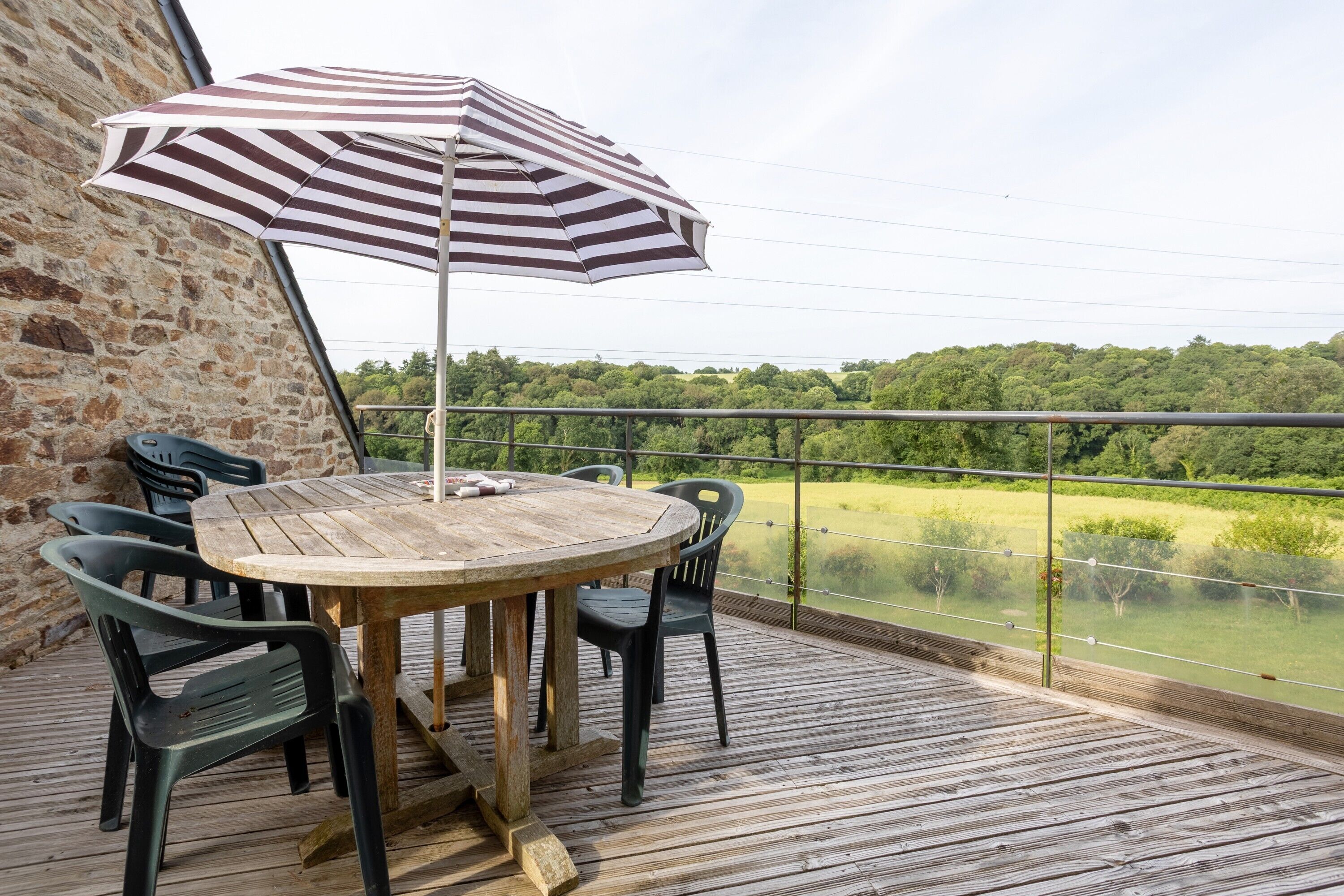 A wooden deck with a round table and chairs, an umbrella, and a view of a green landscape.