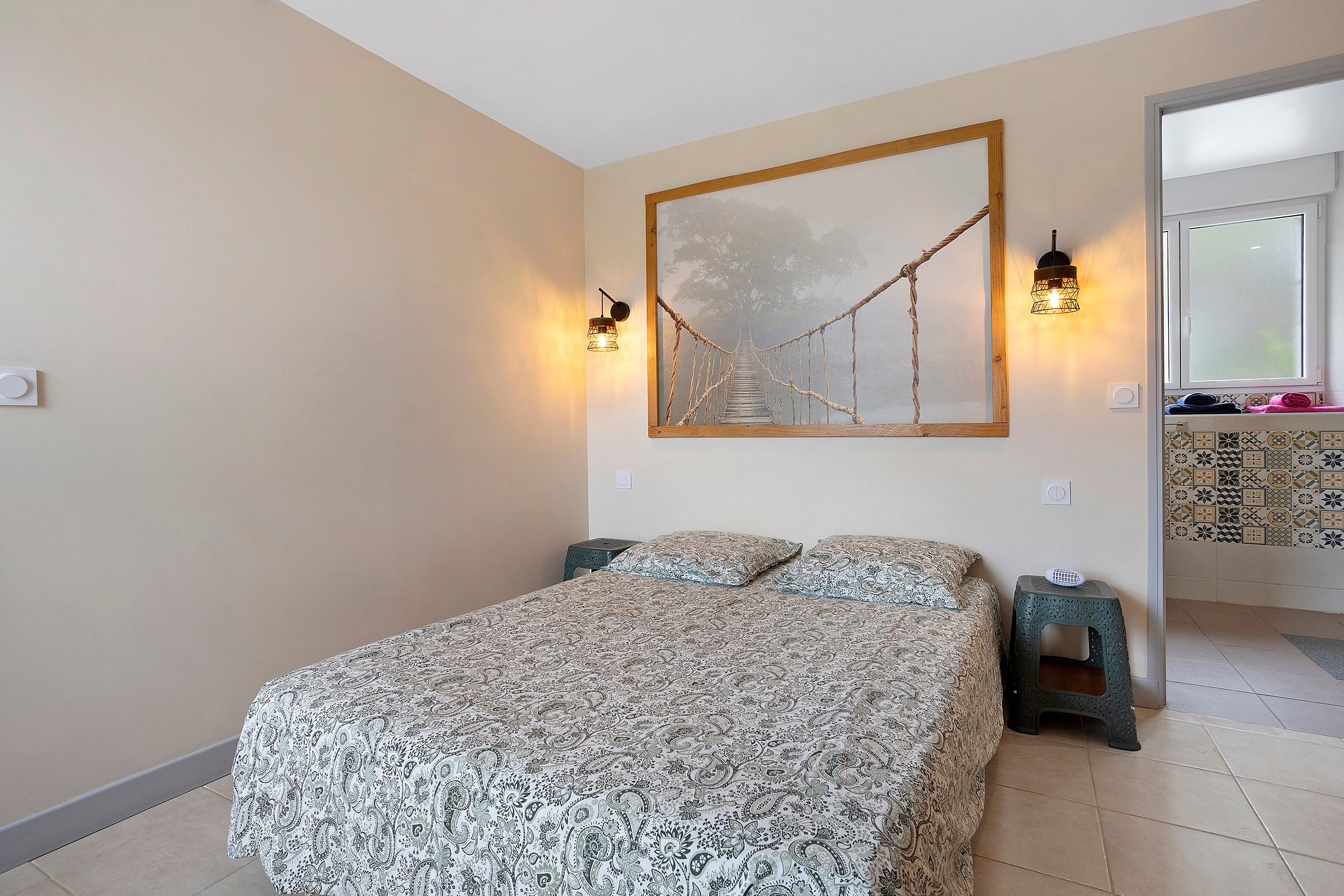 A bedroom with a bed, two nightstands, a wall-mounted lamp, and a framed picture.