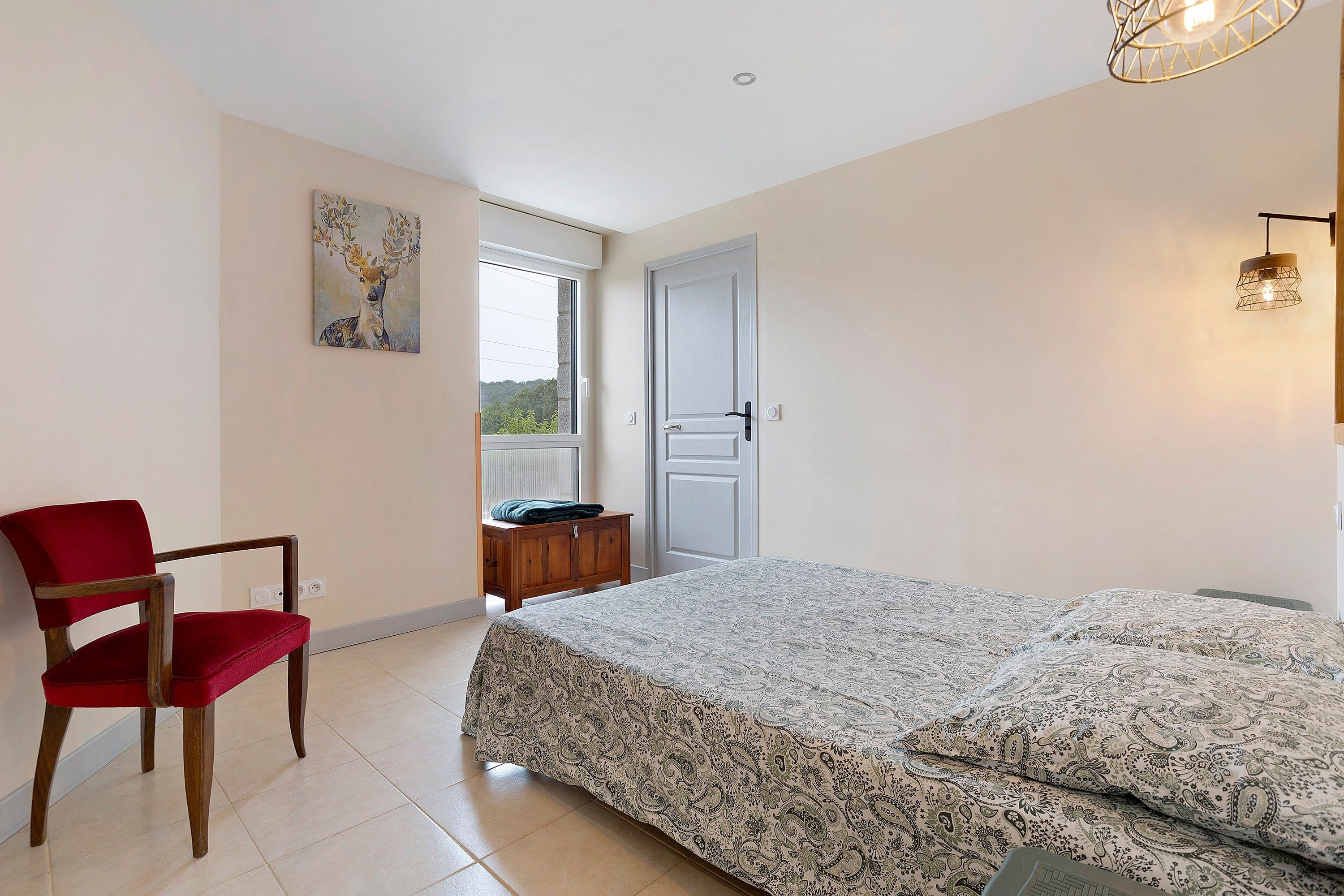 A bedroom with a bed, a chair, a painting, a door, and a window.